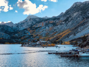 Lake Sabrina near Bishop in fall. Stark granite peaks rise from the shore of the lake as groves of aspen in fall colors cling to the steep sides. Boats docked in the small marina along the shore.