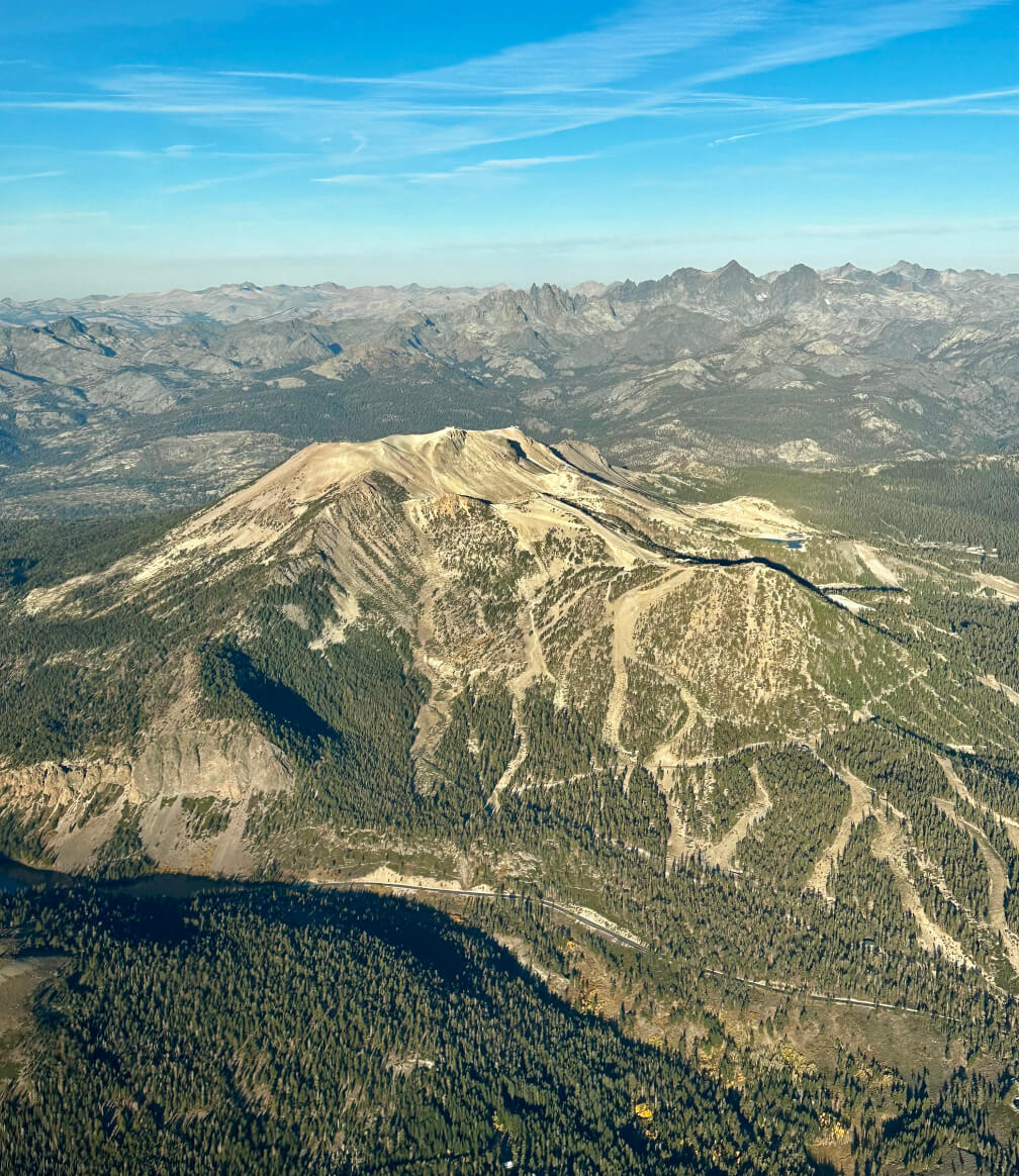 Mammoth Mountain in summer seen from the air, its rounded shape stark contrast to the surrounding jagged peaks